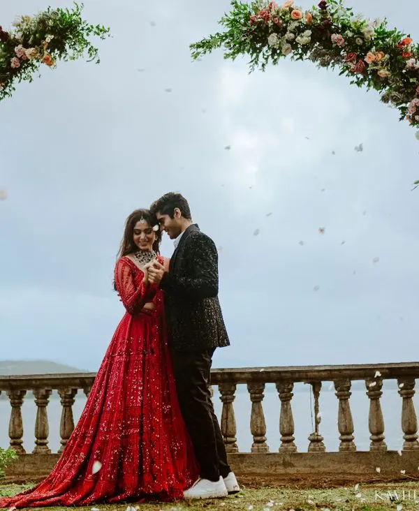 A romantic kiss under a heart-shaped floral arch, set against a serene lake. This is a perfect example of a planned, yet emotionally resonant pre-wedding photograph.