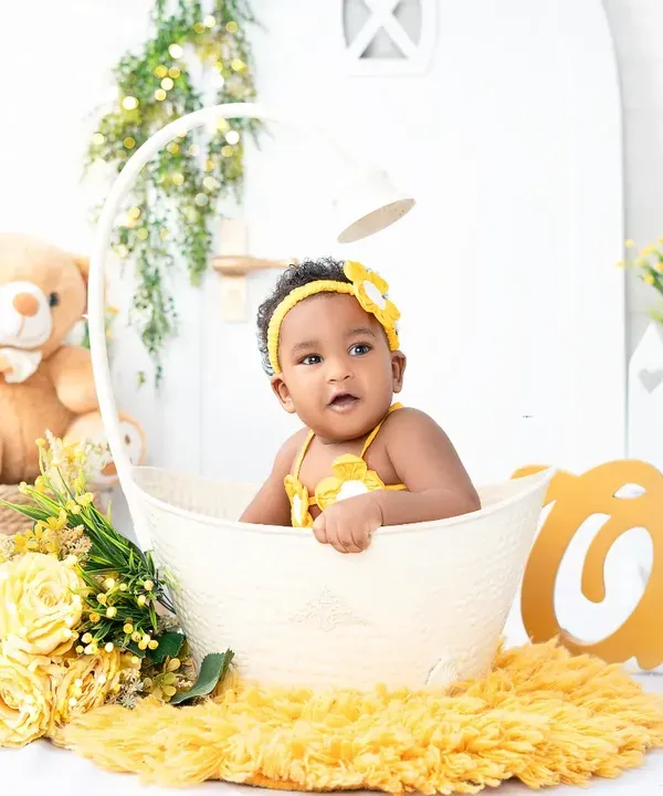 A sweet sitter session portrait of a baby girl in a bright yellow outfit, peeking out of a basket. These sessions are perfect for capturing babies once they can sit up on their own.