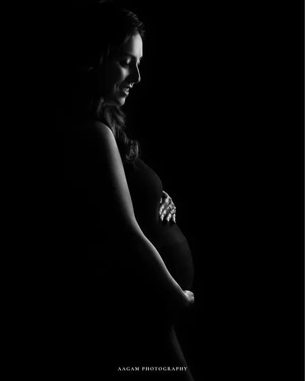A minimalist masterpiece. This low-key silhouette uses a single stream of light to sculpt the beautiful curve of the baby bump, creating a dramatic and artistic portrait.
