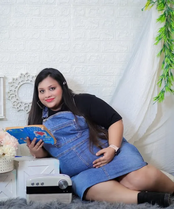 A cozy and casual moment in the studio. The mom-to-be relaxes with a book next to our teepee prop, wearing a comfortable denim overall dress for a relatable and sweet portrait.
