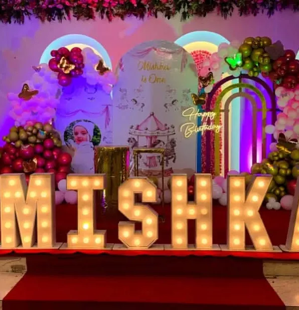 A spectacular first birthday stage for Mishka. This grand setup included large marquee letters spelling her name, a carousel and butterfly-themed backdrop, and multiple balloon arrangements.
