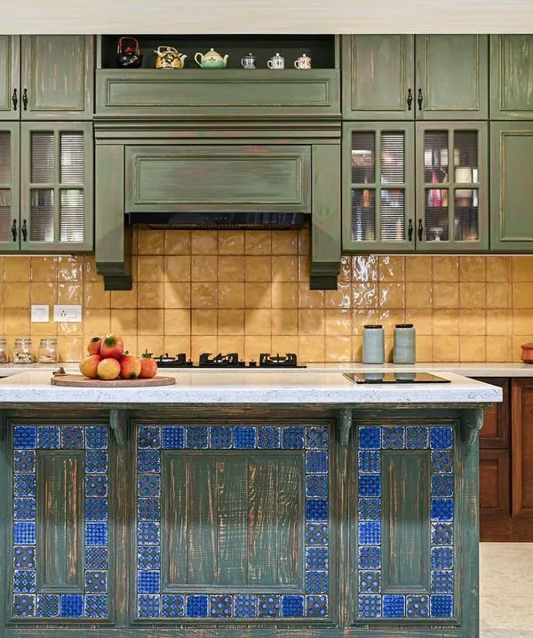 This kitchen is inspired by traditional architecture, with a symmetrical layout and a central island. The distressed olive green shutters, handmade yellow tiles, and vibrant Goan colors create a space full of character and charm.