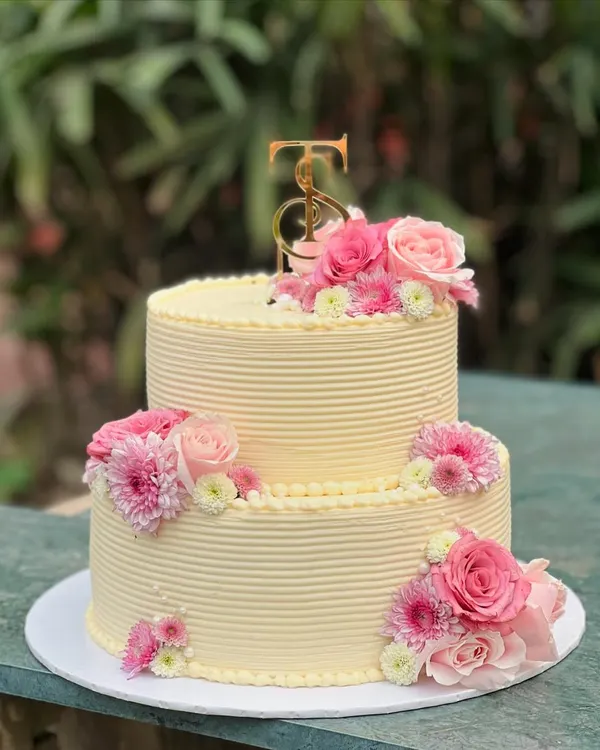 A two-tiered beauty for a grand celebration. This cake features clean, ribbed buttercream frosting and is decorated with cascades of fresh pink flowers for an elegant and timeless look.