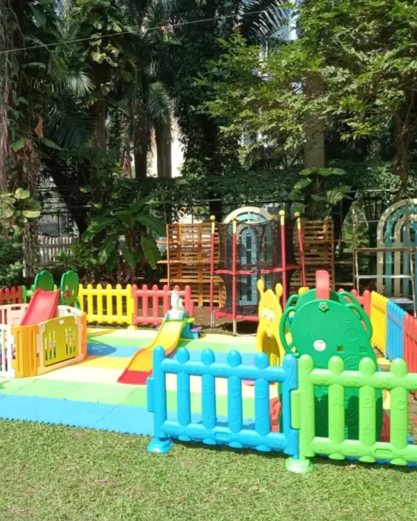 A perfect playzone setup in a lush green garden. This arrangement features multiple slides, climbers, and a rocking horse, all safely enclosed by colorful fencing on soft matting, allowing kids to enjoy the fresh air while they play.