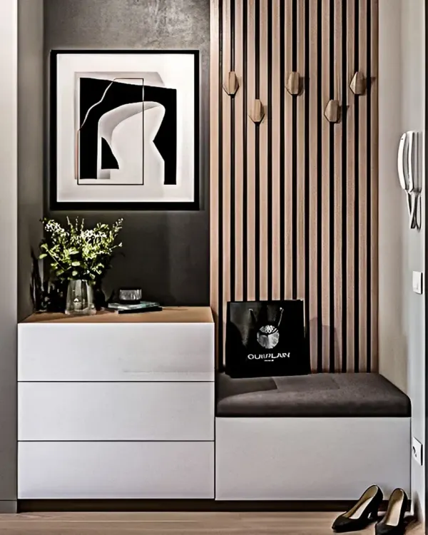 A chic and modern entryway unit featuring a cushioned bench seat, handleless white drawers, and a slatted wood panel with decorative hooks. This design combines style with practical storage.