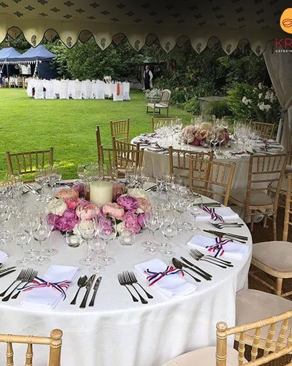 A picture-perfect garden party we catered at a client's farmhouse. The round tables are elegantly dressed with white linens, floral centerpieces, and full place settings for a sophisticated outdoor dining experience.