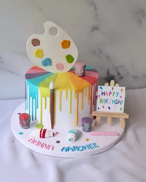 Bringing a splash of color to the birthday canvas. This artist-themed cake features a rainbow drip, an edible paint palette, brushes, and an easel.