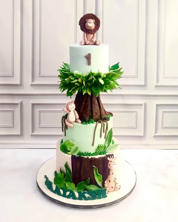 A three-tiered jungle adventure for a first birthday. This cake features a hand-sculpted tree trunk, lush sugar leaves, and adorable fondant animals like a lion, monkey, and giraffe, creating a wild and wonderful centerpiece.