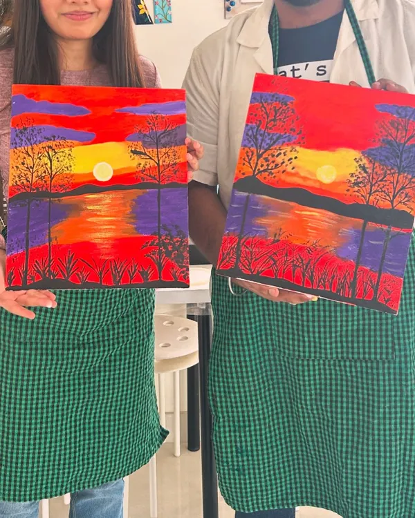 A couple proudly holding their matching sunset paintings. Our guided canvas painting workshops are perfect for beginners and make for a memorable date.