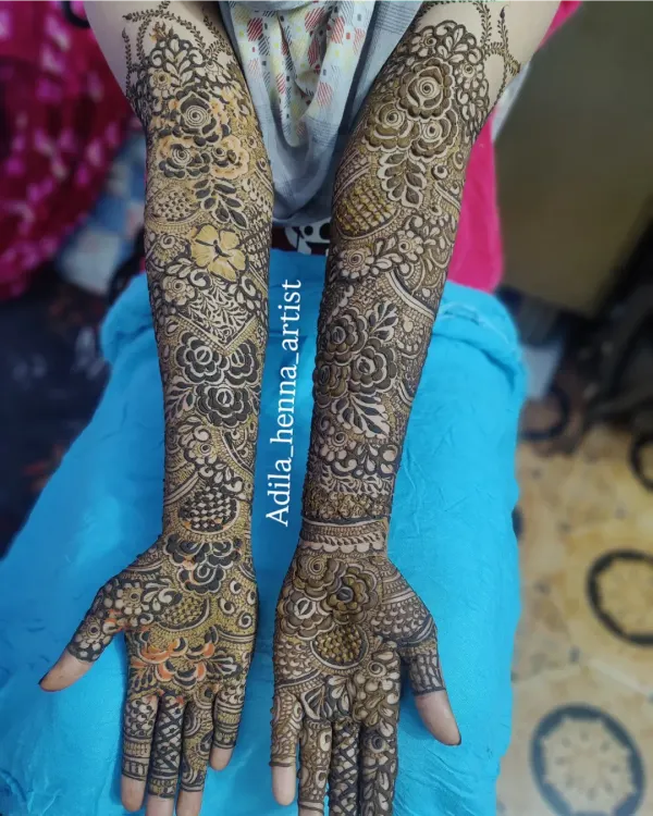 A classic example of full-arm bridal henna, featuring a dense mix of floral, paisley, and geometric patterns. The shading technique adds depth and dimension to the design.