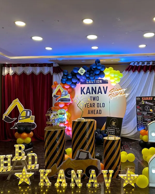 A fun and busy construction theme for a two-year-old. The setup includes caution-striped plinths, excavator cutouts, a personalized 'Caution' sign, and a yellow and black balloon arch.