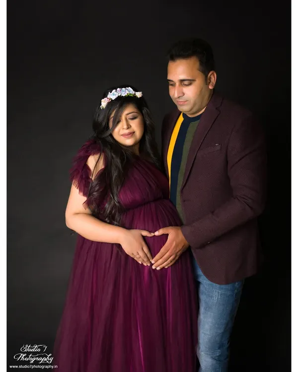 A classic studio portrait of a couple celebrating their growing family. The simple dark background and professional lighting ensure the focus is entirely on their joy and connection.