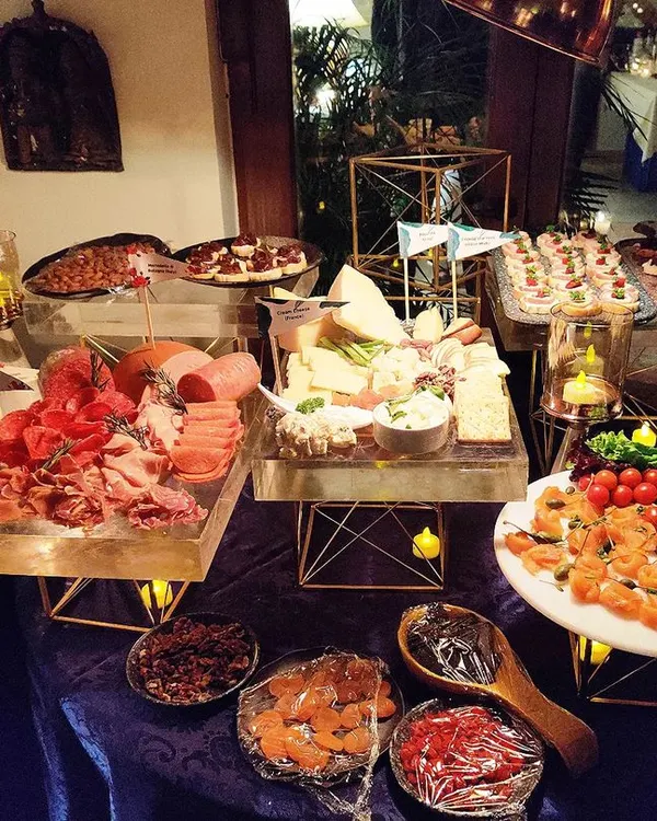 An elaborate cheese and charcuterie grazing table for an intimate gathering. The spread includes a variety of cured meats, artisanal cheeses, dips, and canapés, beautifully arranged with candelabras for a warm, inviting ambiance.