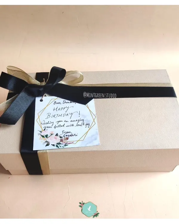A beautifully wrapped birthday hamper. The simple, elegant box is tied with a black satin ribbon and features a handwritten note, ready to create that "wow" moment.