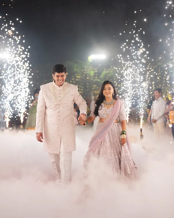 A grand entrance for a beautiful couple. The bride's reception makeup was designed to be luminous and elegant, complementing her sparkling lavender lehenga for a truly magical walk among the smoke and sparklers.