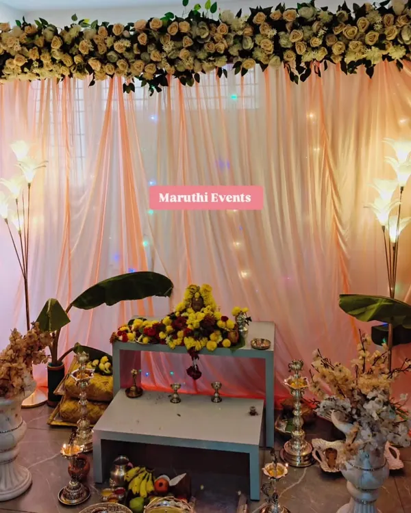 An elegant and serene setup I created for a Gauri Maa puja at home. The decor features a lush overhead arrangement of artificial cream roses, soft peach drapery, and traditional elements like banana leaves and diyas.