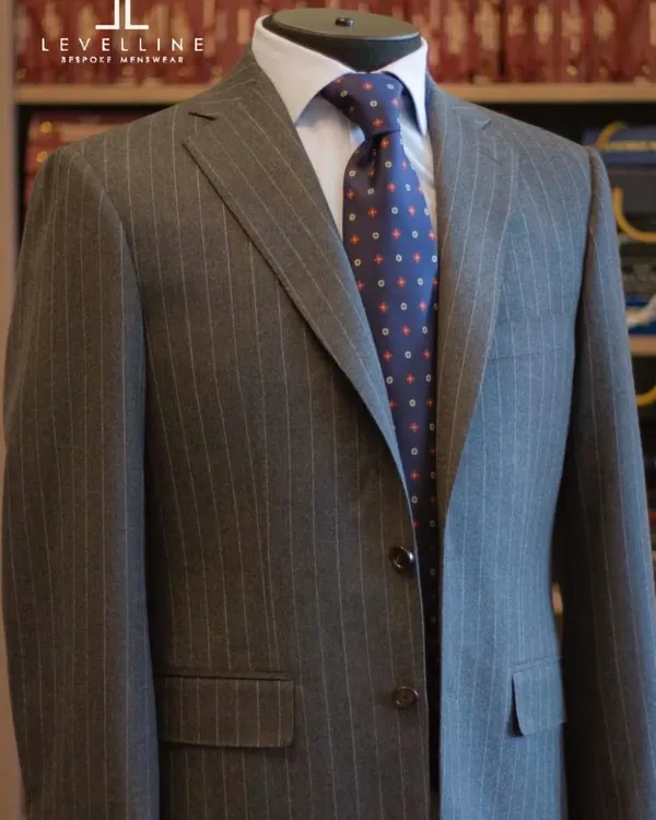 A grey pinstripe suit is a cornerstone of any professional wardrobe. This two-button suit, crafted from 130's count wool, offers a classic silhouette with the unmatched quality of a bespoke fit.