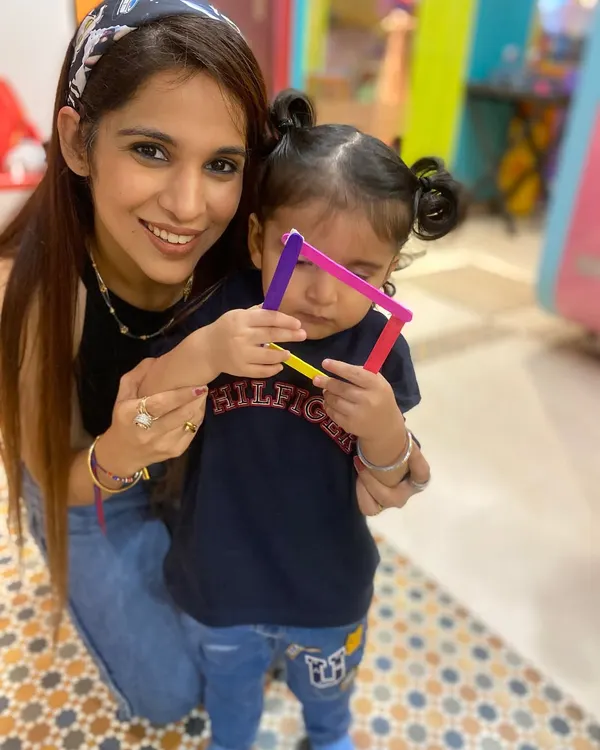 A mother and her child proudly display a shape they created with colorful popsicle sticks. This simple activity helps with learning shapes and colors while strengthening the parent-child bond.