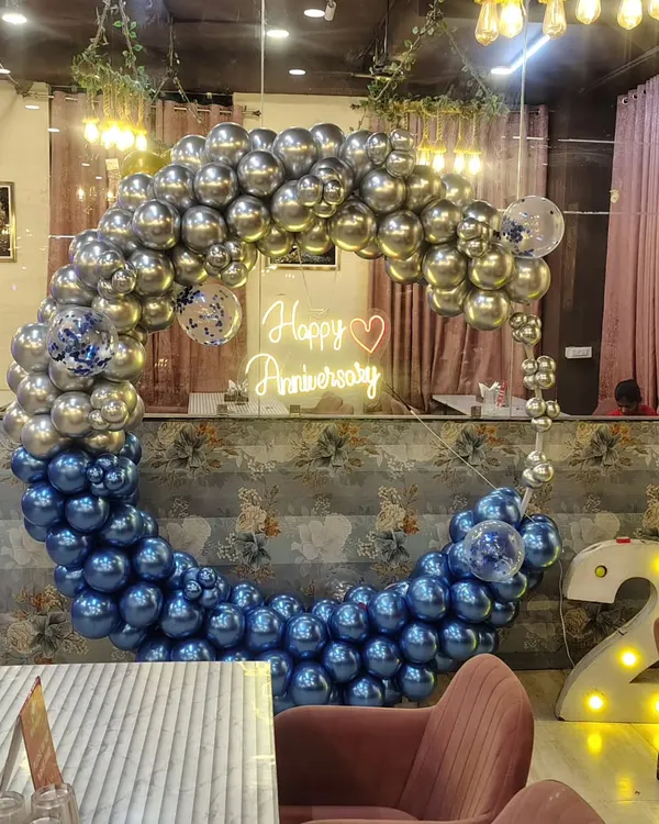 This anniversary backdrop features a stunning balloon ring made of metallic silver and chrome blue balloons. A "Happy Anniversary" neon sign in the center adds a warm glow, making it a perfect photo spot for the happy couple.