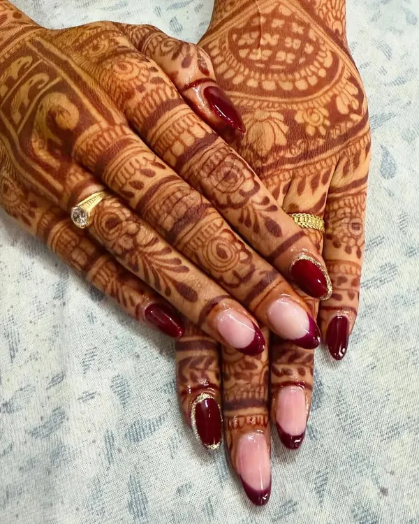 For a bride, hands are always in the spotlight. I designed these deep red almond-shaped nails with a reverse French manicure style to beautifully complement the intricate details of the wedding mehndi.