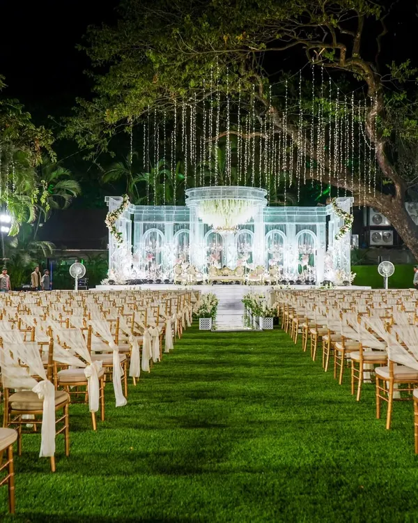 A glimpse into the dream weddings I help create. This stunning outdoor lawn setup in Mumbai, with its crystal-clear stage and hanging lights, shows how I can transform any space into a magical venue for your big day.