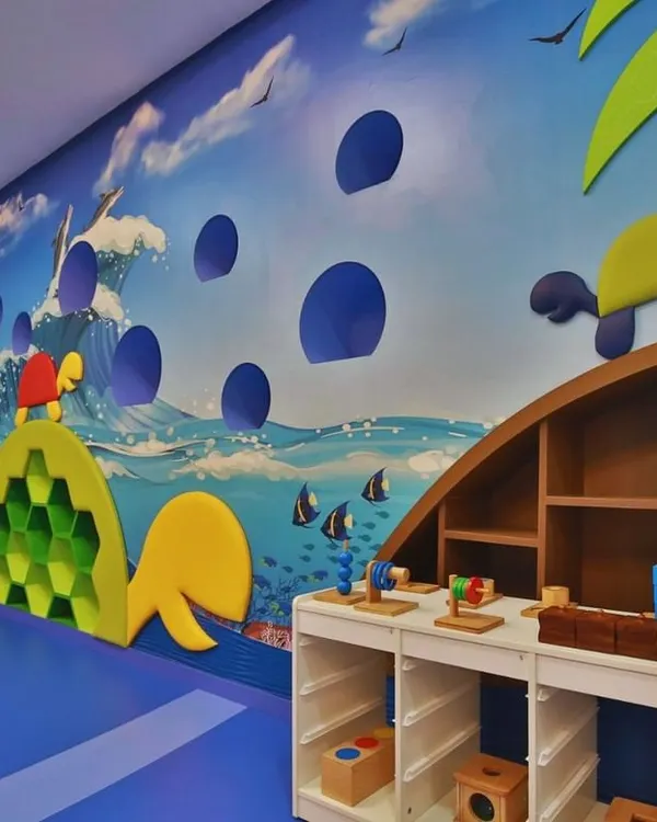 This ocean-themed classroom at Supaksha features a turtle-shaped climbing wall and custom low-height tables for hands-on activities. The entire space is designed to be an interactive learning habitat.
