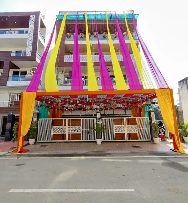 A full view of a multi-story house decorated for a wedding. I use long, flowing drapes in bright yellow and pink that run from the rooftop down to the entrance canopy, making a big visual impact.