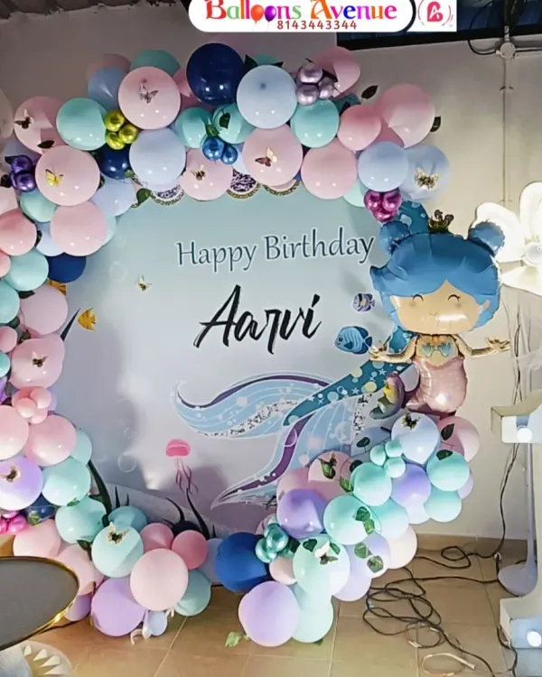 A beautiful mermaid-themed first birthday party for Aarvi. This setup features a circular backdrop with a custom design, a full balloon garland in ocean colors, and a large light-up number '1'.