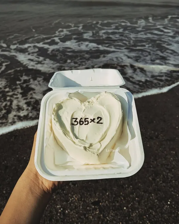 A simple and aesthetic heart-shaped bento cake for a second anniversary, pictured against a beautiful beach backdrop. It's all about creating special moments.
