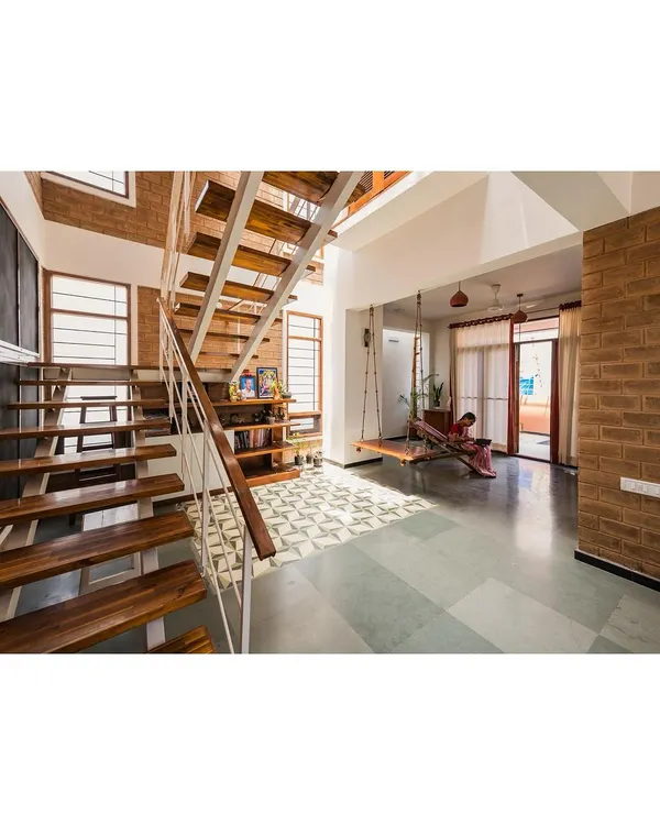 This is the heart of a home we designed, where natural light, earthy materials, and open spaces come together. We used exposed brick and Kota stone flooring to create a warm, honest feel, while the floating wooden staircase and traditional swing add a sense of lightness and play.