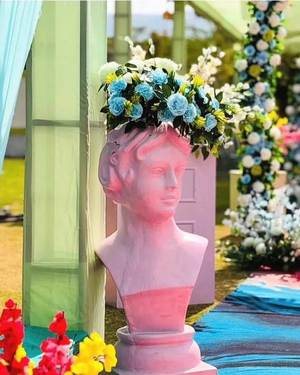 A quirky decor detail featuring a pink bust statue used as a vase for a vibrant blue floral arrangement.