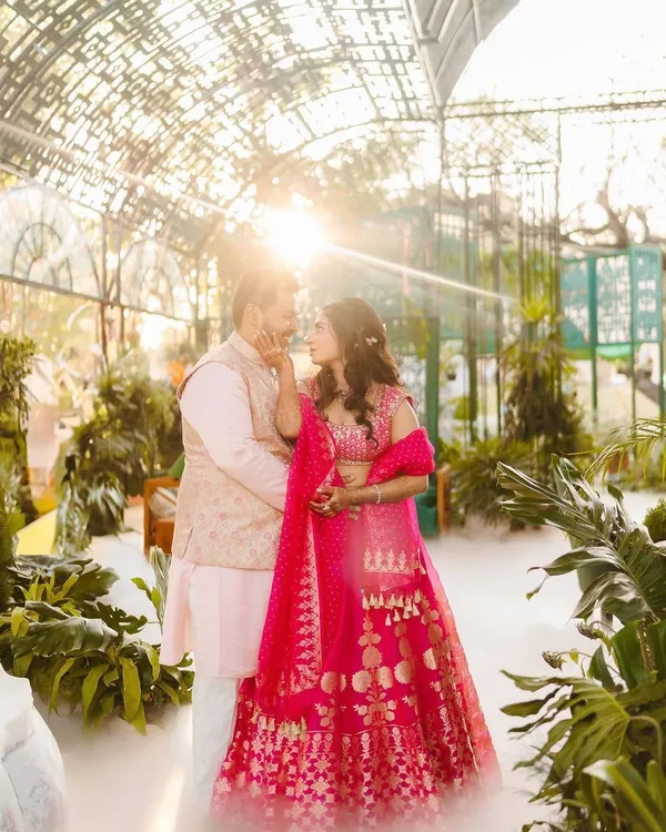 A dreamy, sun-kissed shot of Shree and Abhishek at their Mehendi. Shree is wearing a vibrant pink Anita Dongre lehenga, which looks stunning in the greenhouse setting.