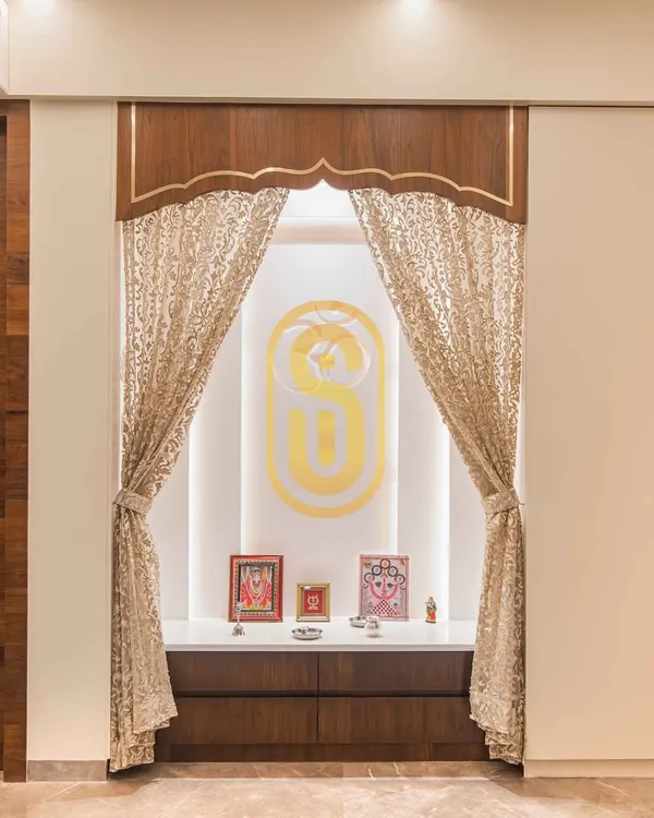 A beautifully crafted pooja unit designed as a serene and sacred space within the home. It features intricate woodwork, elegant curtains, and soft backlighting to create a peaceful ambiance.