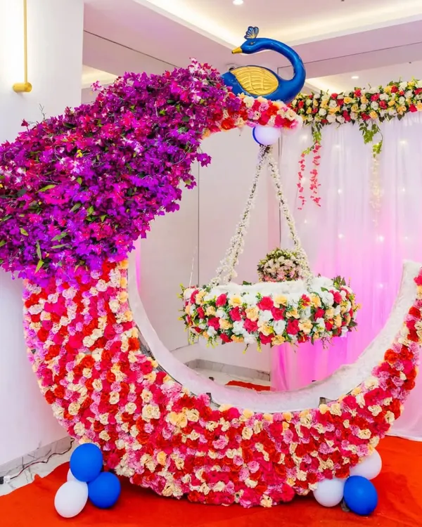 A beautiful naming ceremony setup featuring a large floral moon cradle, a signature piece for welcoming a new baby. This elegant design combines fresh flowers and a peacock motif, creating a perfect photo opportunity for your baby's 'barsa' or naming function.