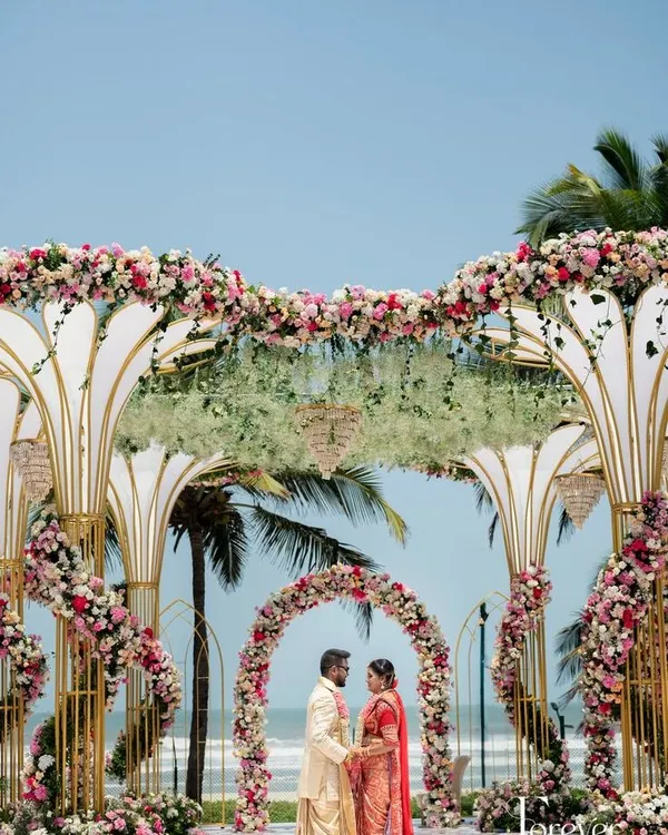 A truly grand mandap for a beach wedding, featuring intricate, large-scale structures adorned with pink and white florals against the ocean backdrop. This design is for couples who want their wedding ceremony to be a statement of pure luxury.