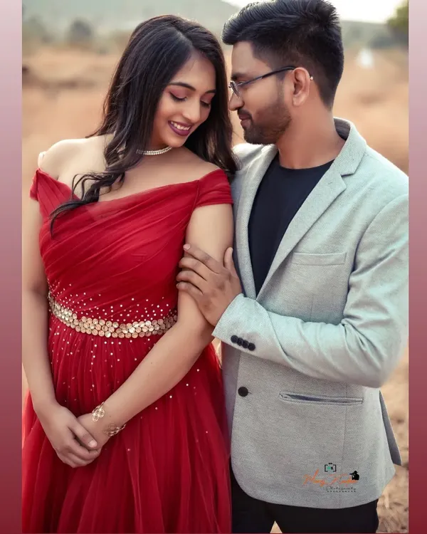 A tender moment between a stylish couple. Her off-shoulder red gown with a sparkling belt pairs beautifully with his light grey blazer for a modern pre-wedding look.