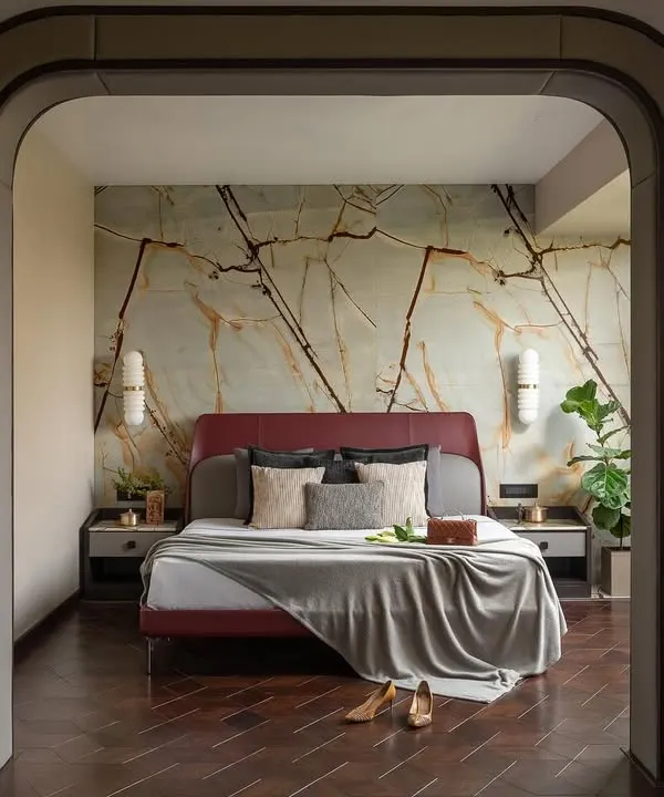 I designed this master retreat as a realm of understated elegance. Passing through the archway, you are greeted by a sanctuary of muted hues and natural textures, where a maroon bed against a cool marble wall invites blissful slumber.