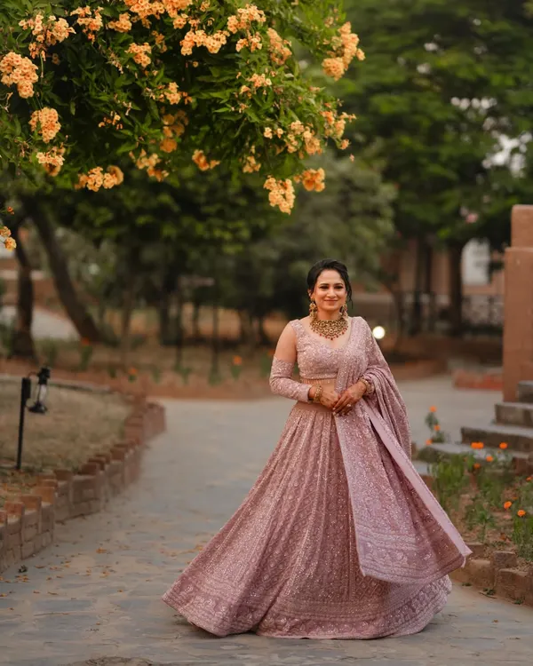 A full-length portrait of the bride, Raman, in her stunning lavender engagement lehenga. The flowering trees at Gaj Resort provide a beautiful, natural frame for this elegant shot.