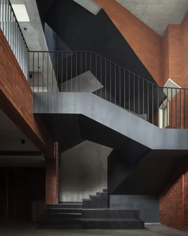 The central staircase of the Brick House is a non-linear journey through the home. Its sharp, geometric forms in black pigmented plaster create a powerful contrast with the warmth of the exposed brick walls.