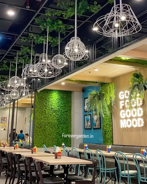 A cafe interior featuring a moss wall, hanging plants, and a "Good Food Good Mood" neon sign. This project shows how greenery can be integrated with branding to create a cohesive and inviting atmosphere.