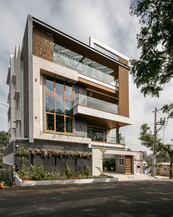 A daytime view of the Hennur Road residence, showcasing the interplay of Italian marble cladding, WPC vertical screens, and large glass windows. The design maximizes the wide frontage to create a facade that is both elegant and imposing.