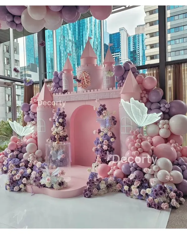 A breathtaking princess castle backdrop in shades of pink and lavender. This elaborate setup is adorned with cascading flowers, balloon garlands, and glowing butterflies, creating a real-life fairy tale for a first birthday.