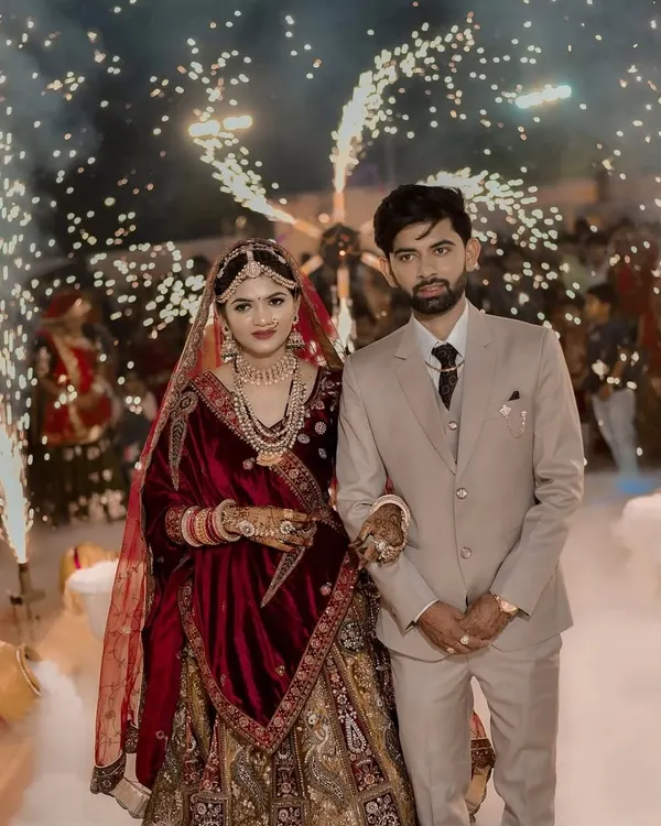 A professional photograph capturing a couple's reception entry. They are surrounded by a dense floor of white fog and framed by brilliant cold pyro sparklers, creating a high-contrast, dramatic image.