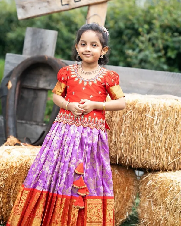 This little one looks absolutely radiant in her custom Kanchi Pattu lehenga. The vibrant red and purple combination is perfect for festive occasions.