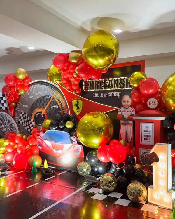 A complete Ferrari-themed first birthday stage with a race track floor, light-up number "1", and a personalized backdrop.