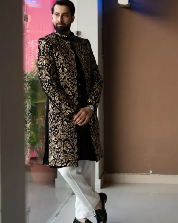 A masterpiece of fusion wear. This black sherwani is covered in dense, intricate gold floral embroidery, paired with classic white trousers for a look that is both royal and contemporary.