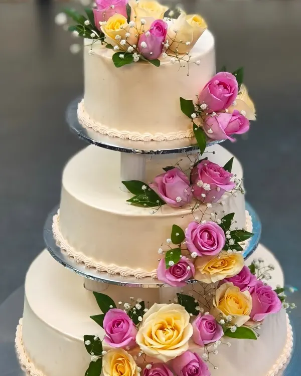 We believe your wedding cake should be as grand as your love story. This classic three-tiered cake, adorned with fresh pink and yellow roses, is a timeless centerpiece for any wedding celebration.