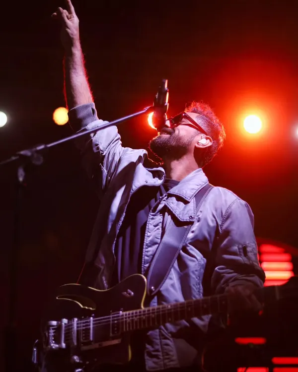 A guitarist reaching for a high note, one hand raised in sync with the music's peak. This is an action shot that freezes the climax of a song.