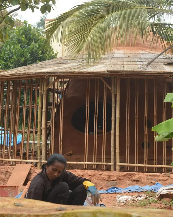 An exterior view of the Cheerville farmhouse under construction. This image shows the integration of a bamboo framework with earthen walls, showcasing a hybrid approach to sustainable building.