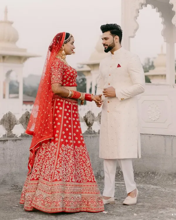 A picture of pure happiness. Our groom Abhilash looks dashing in a classic ivory sherwani, perfectly complementing the bride's vibrant red lehenga.